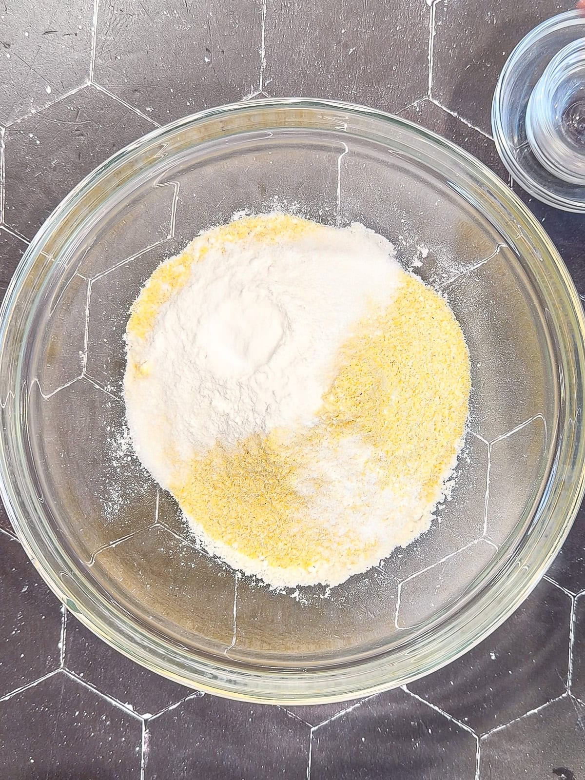 Dry ingredients for cornmeal waffles in a glass bowl.