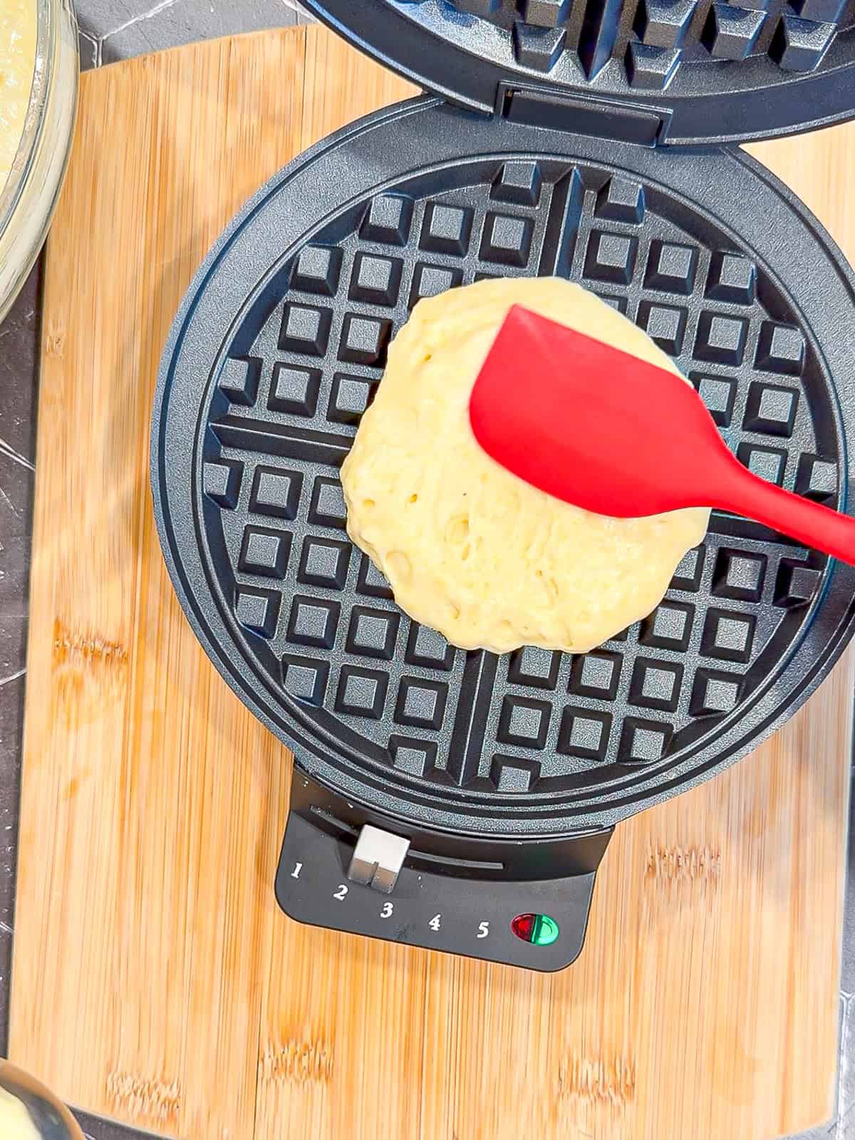 Using a spatula to spread waffle batter out in a waffle maker.