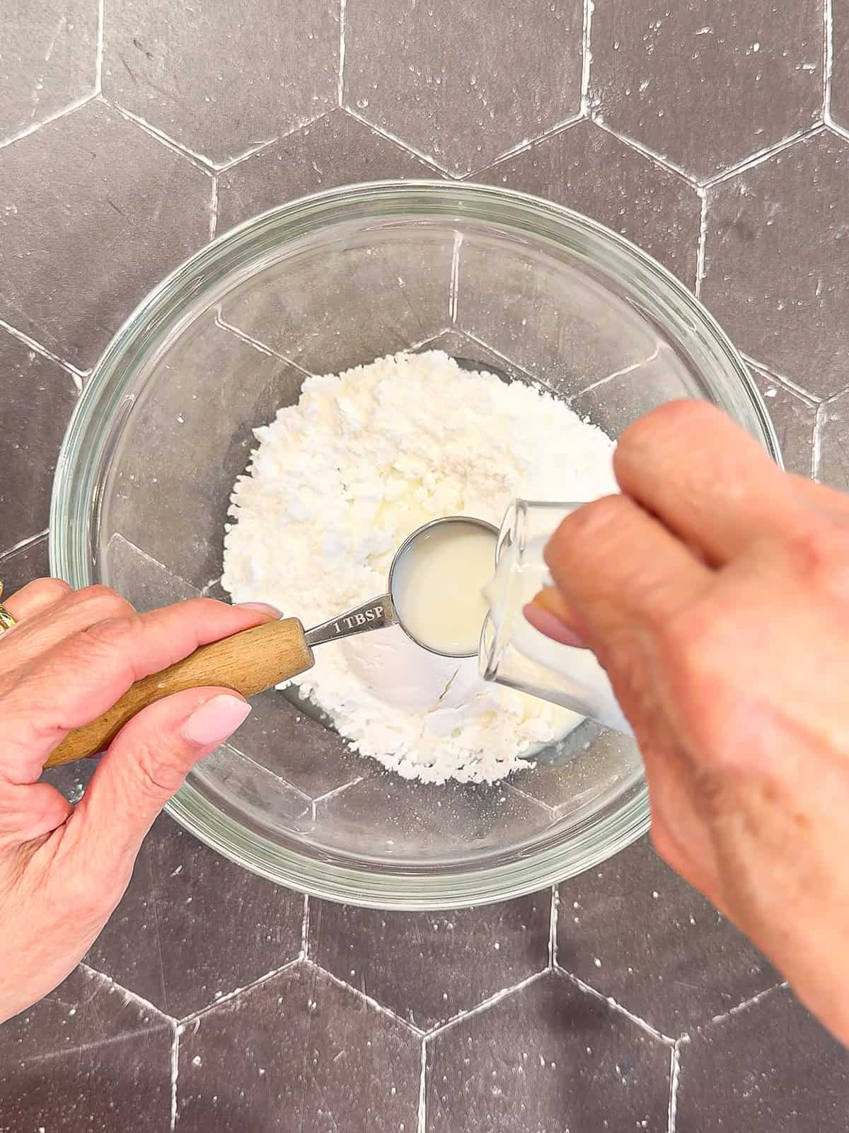 Adding milk and lemon juice to powdered sugar in a glass bowl.