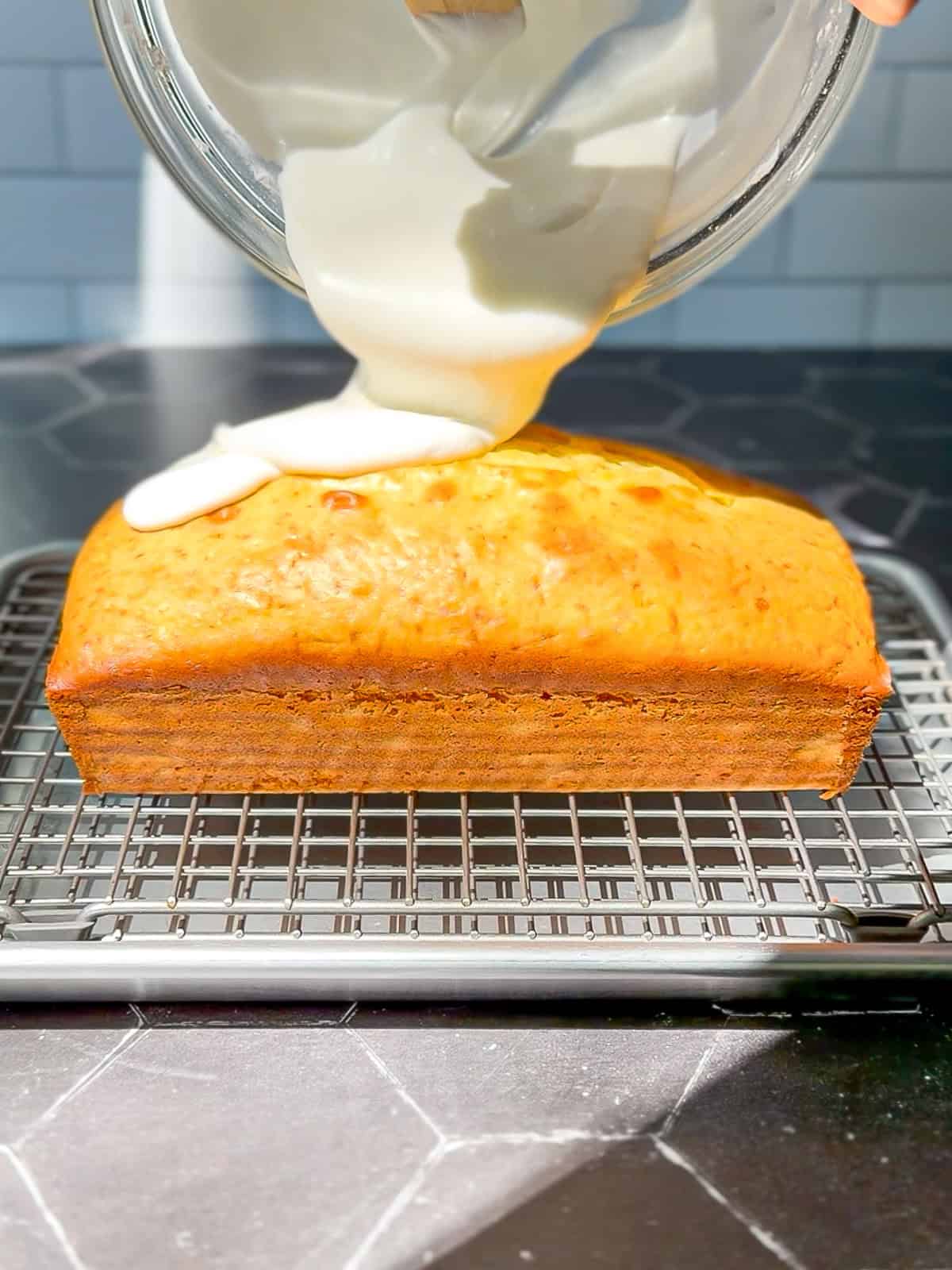 Pouring lemon glaze on top of a loaf cake sitting on a wire rack.