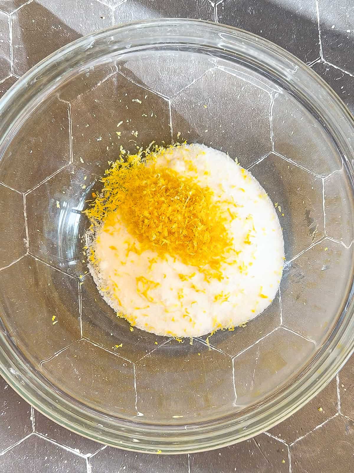Lemon zest and granulated sugar in a glass bowl.