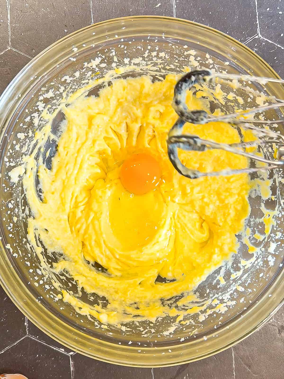 Adding an egg to wet ingredients in a glass bowl.