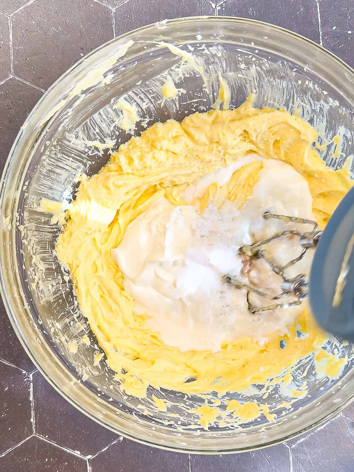 Using a hand mixer to mix lemon loaf cake batter in a glass bowl.