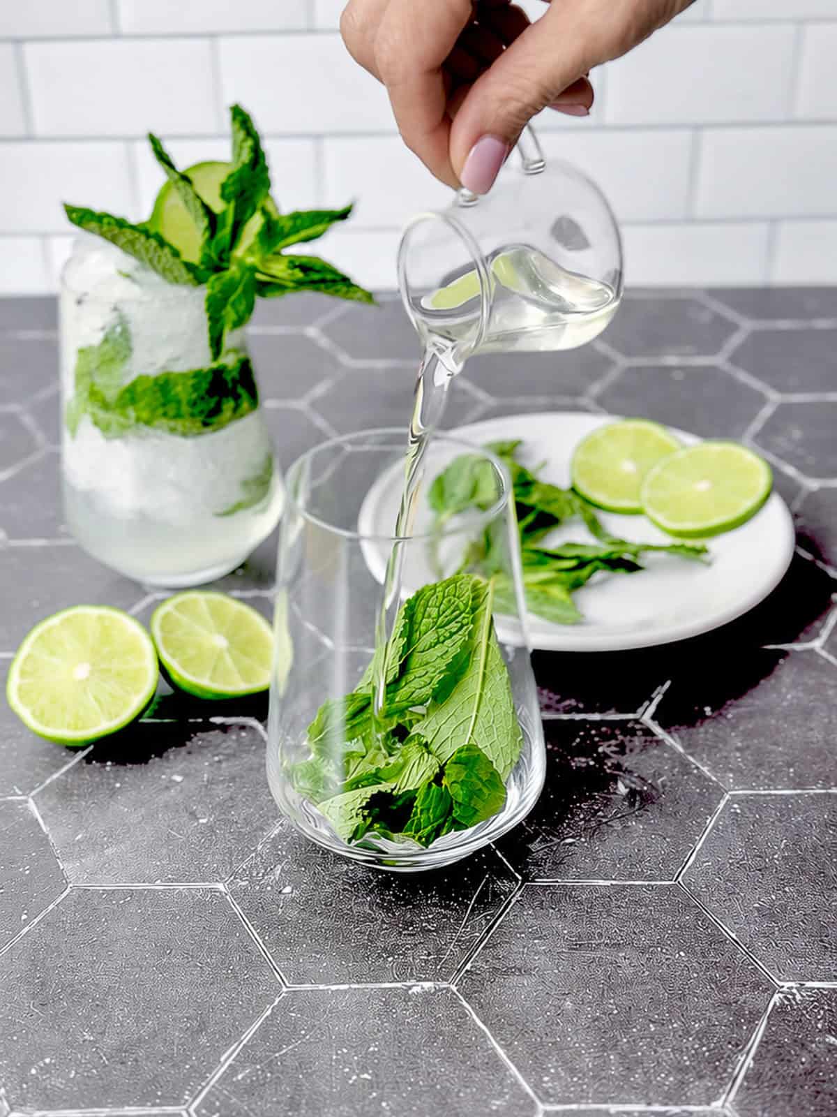 Pouring a simple syrup over Mint leaves in a cocktail glass.