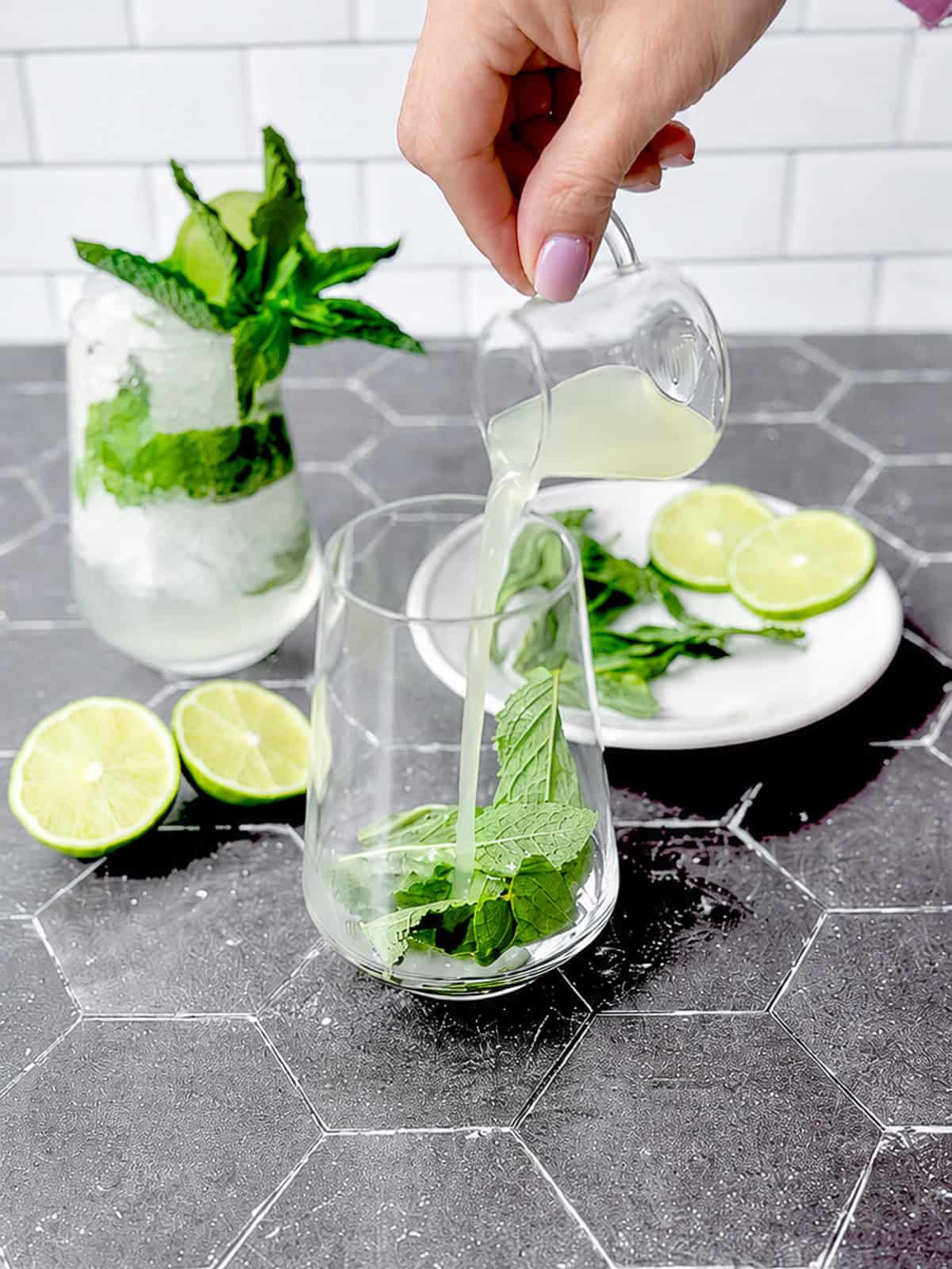 Pouring lime juice over Mint leaves in a cocktail glass.