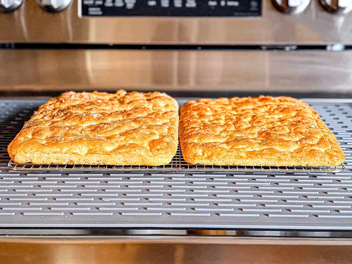 Two focaccia on a wire rack on a stove top.