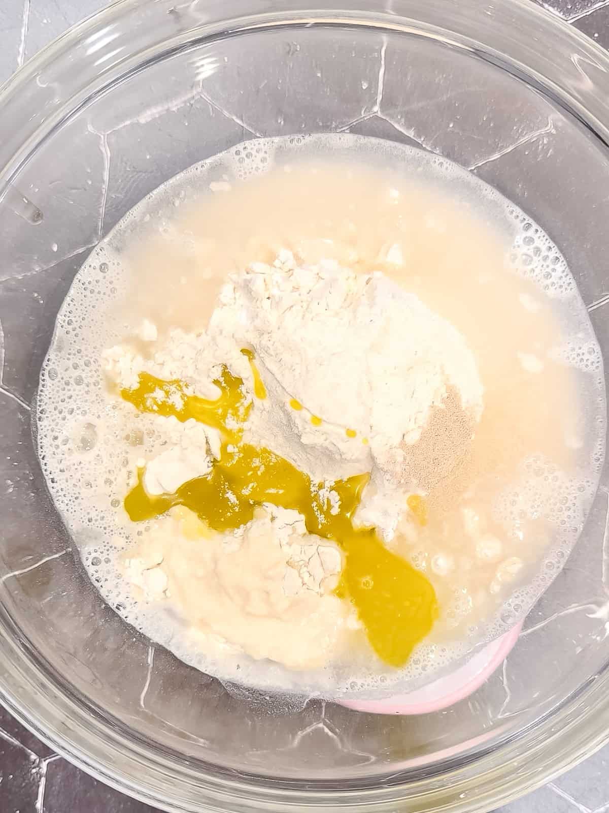 Water and olive oil mixed with dry ingredients in a glass bowl.