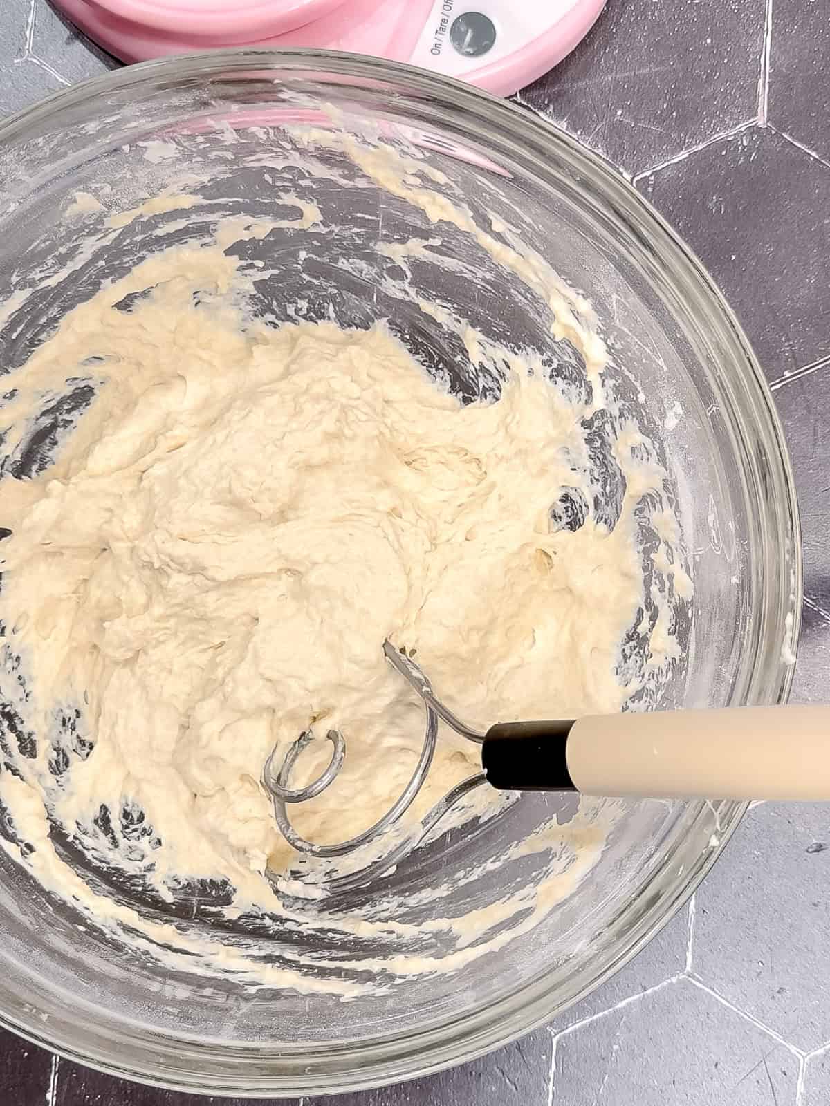 Using a dough whisk to mix focaccia dough in a glass bowl.