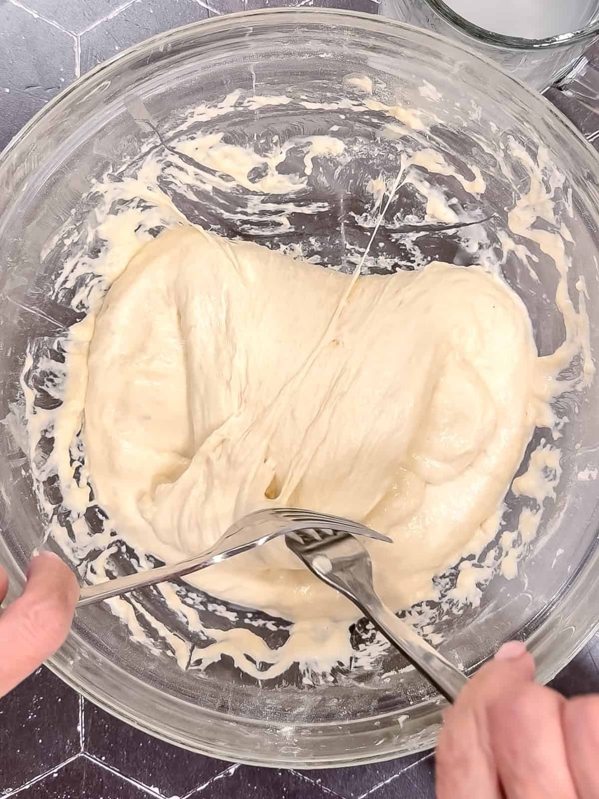Using two forks to fold focaccia dough over onto itself in a glass bowl.