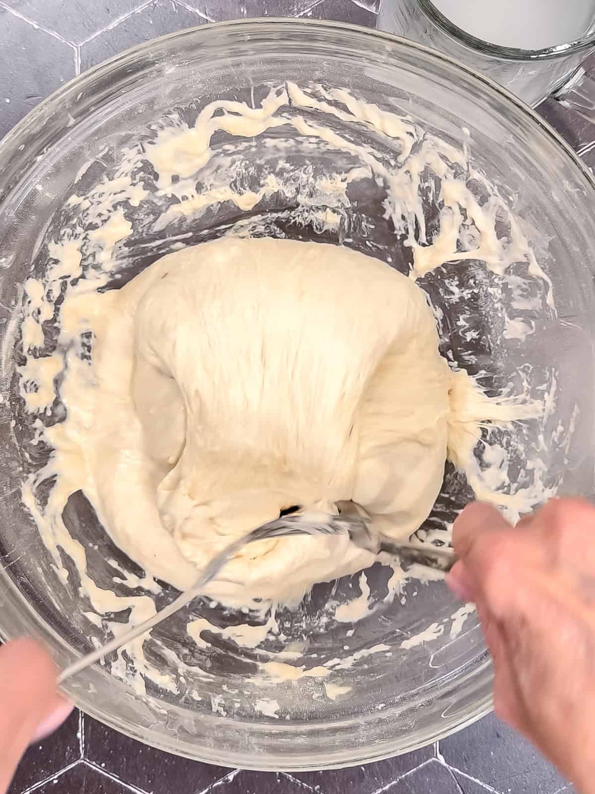 Using two forks to fold focaccia dough over onto itself in a glass bowl.