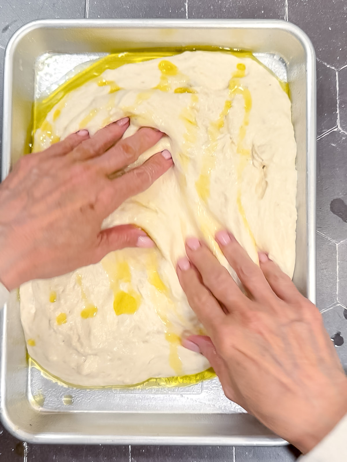 Using fingers to spread focaccia dough in a small sheet pan.