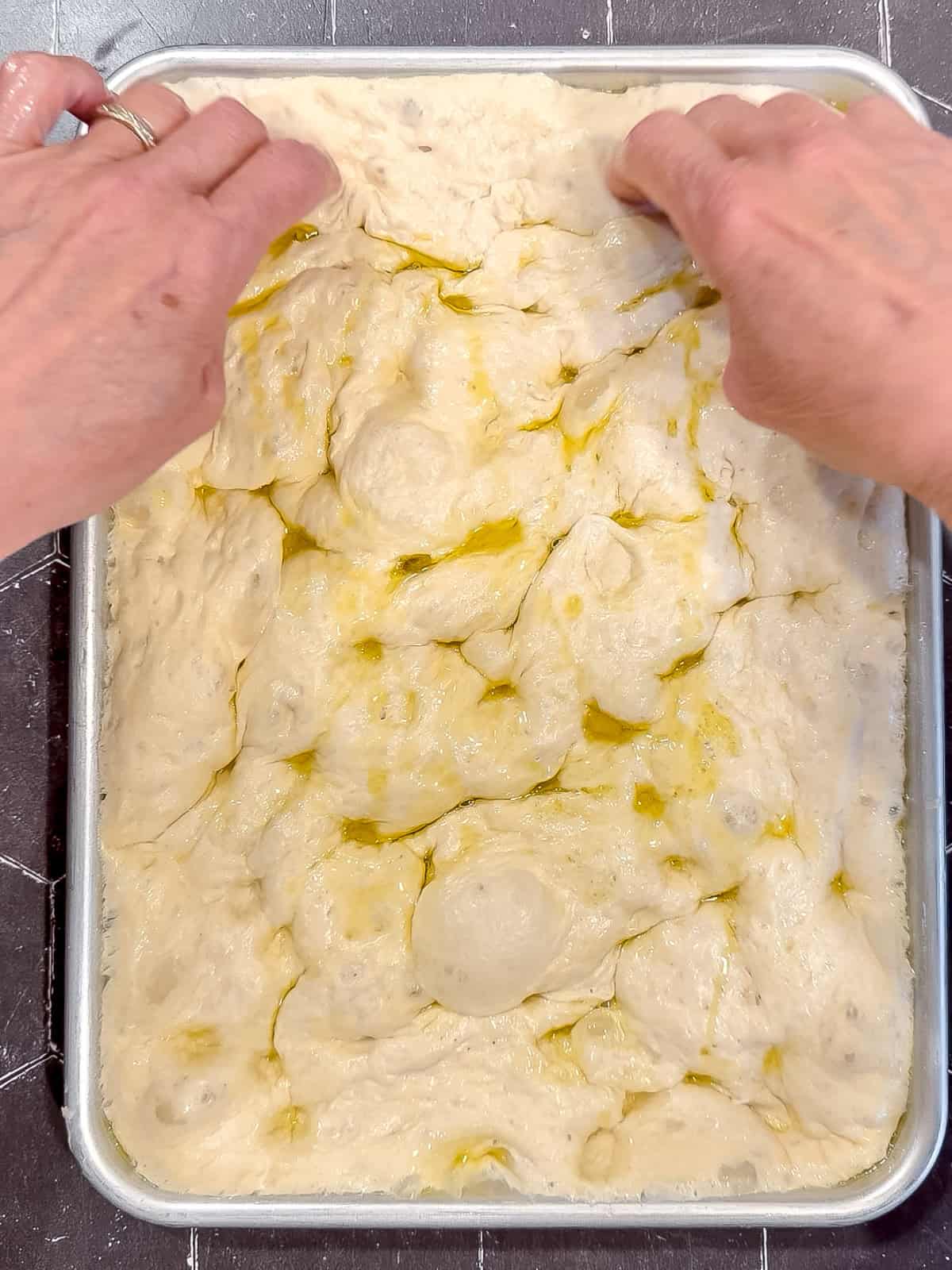 Using fingers to dimple the top of focaccia.