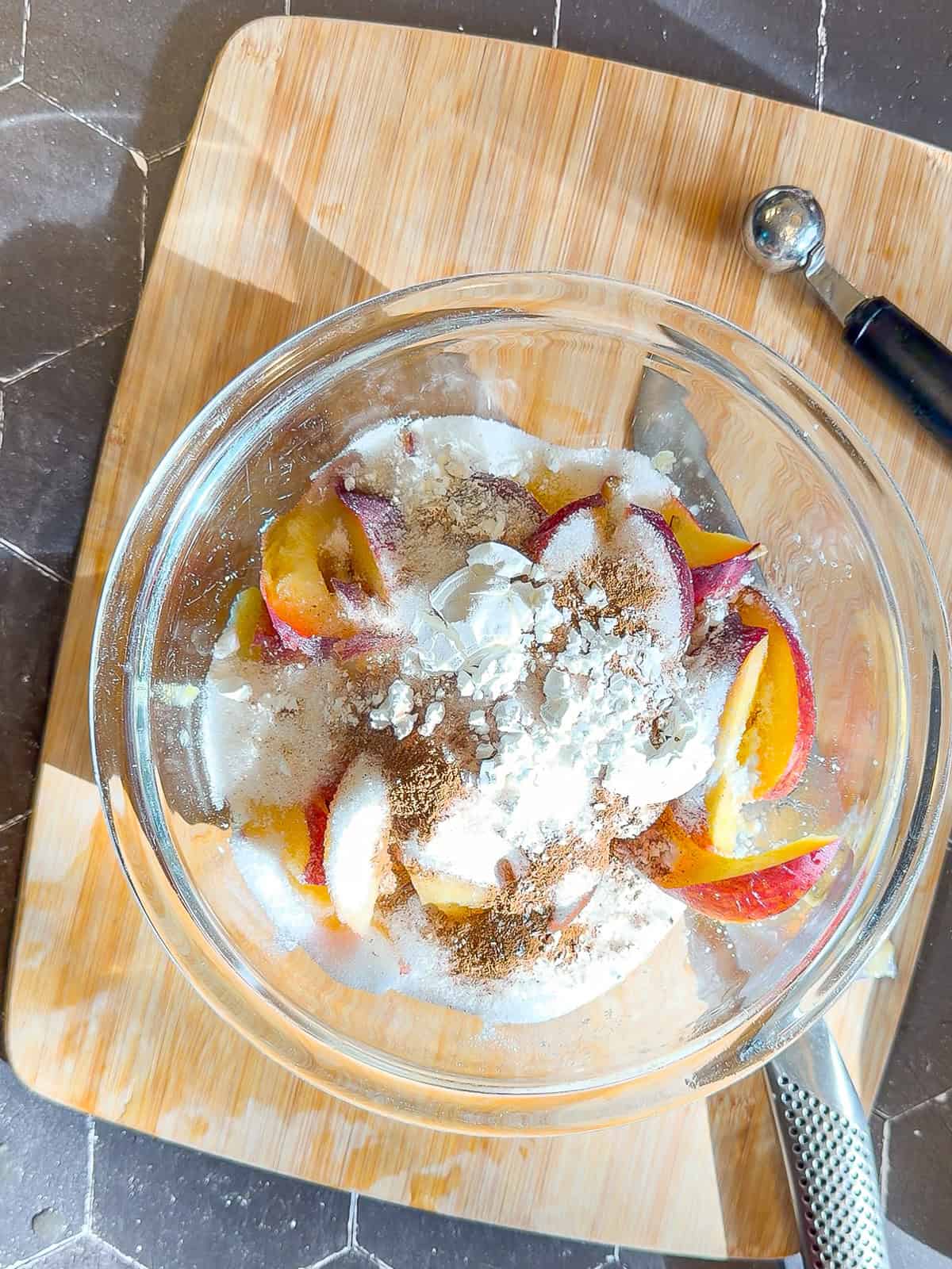 Peaches, sugar, cinnamon, and cornstarch in a glass bowl.