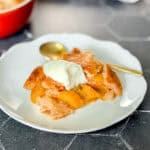 Peach cobbler with a dollop of sweetened yogurt on a white plate.