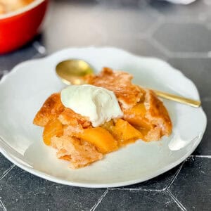 Peach cobbler with a dollop of sweetened yogurt on a white plate.