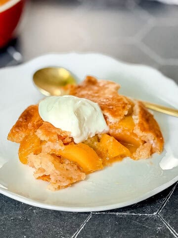 Peach cobbler with a dollop of sweetened yogurt on a white plate.