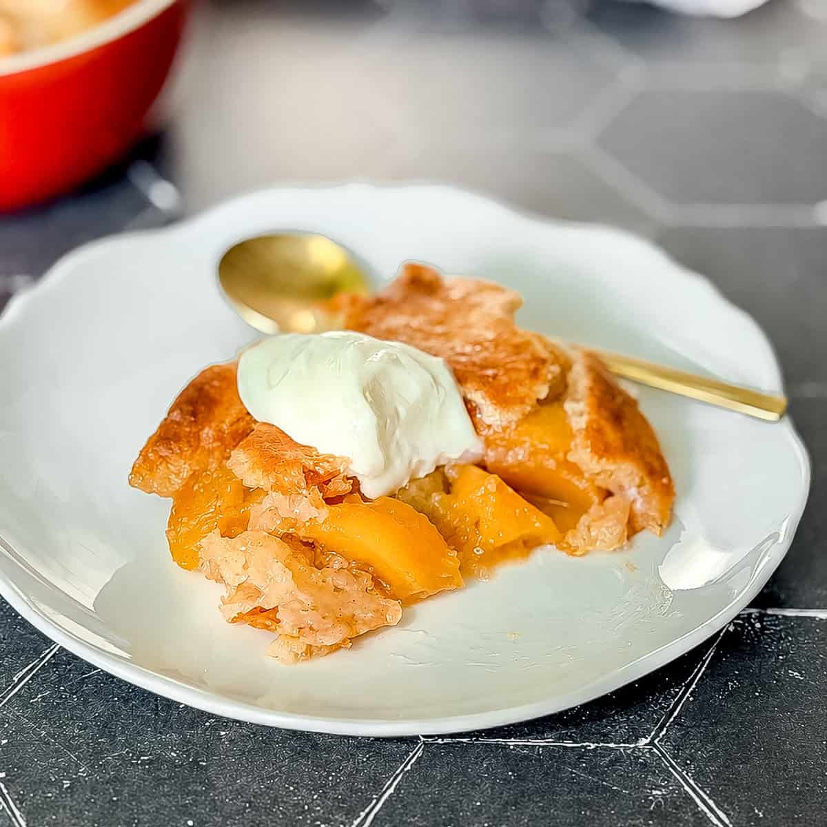 Peach cobbler with a dollop of sweetened yogurt on a white plate.