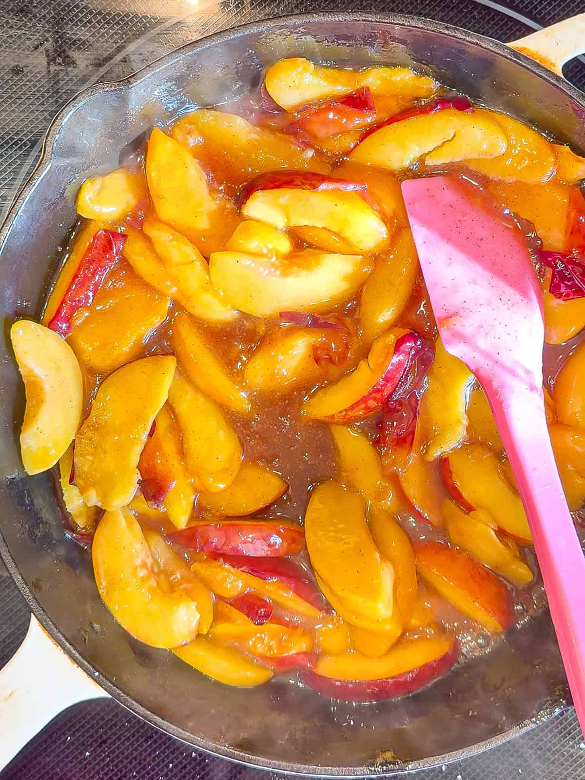 Softening peaches in a cast-iron pan with a pink spatula.