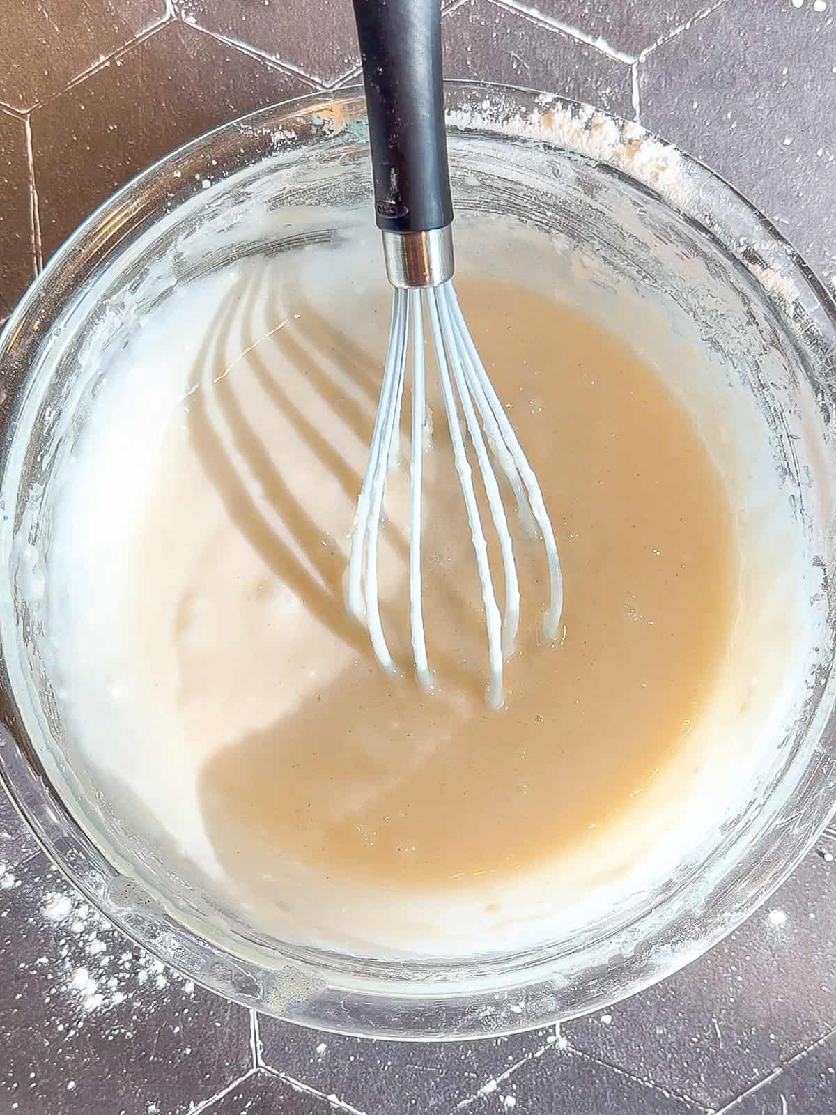 Peach cobbler batter and a whisk in a glass bowl.