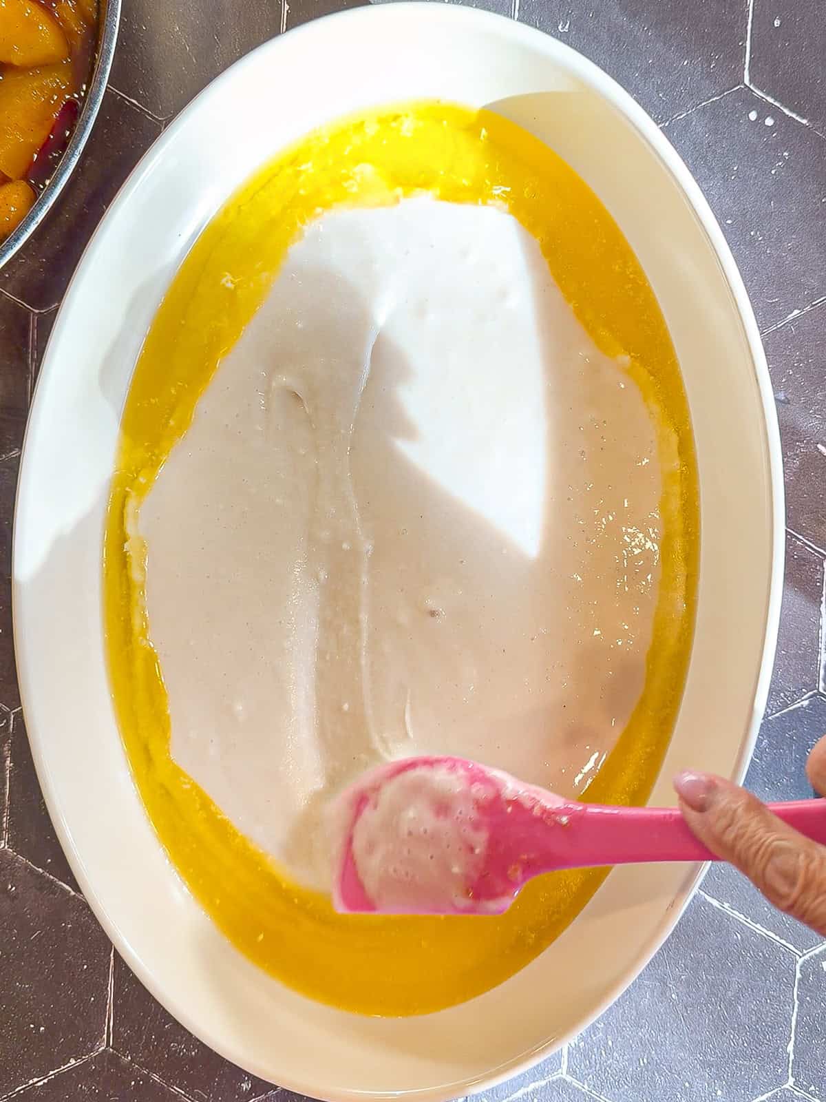 Spread spreading batter in an oval baking dish containing melted butter.