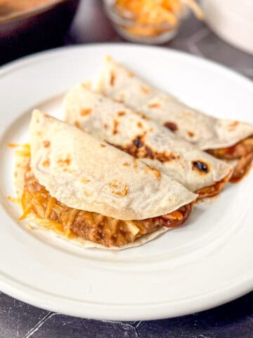 Three bean and cheese tacos on a white plate.