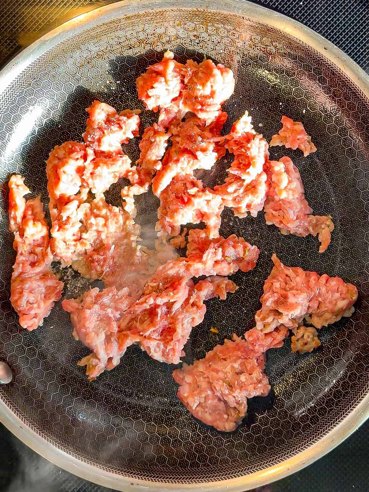 Cooking Italian sausage in a black pan.