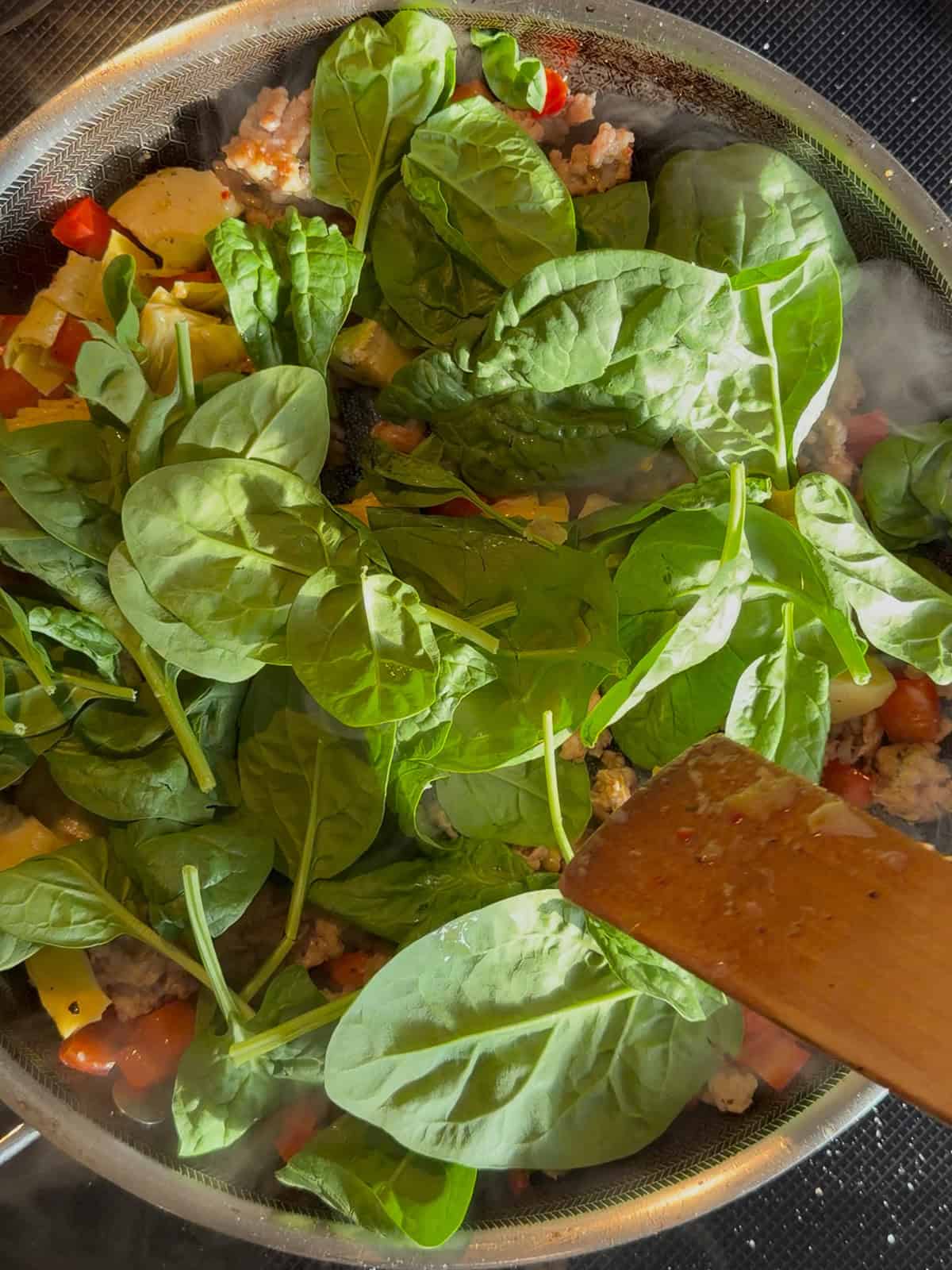 Adding spinach to other ingredients in a black pan.