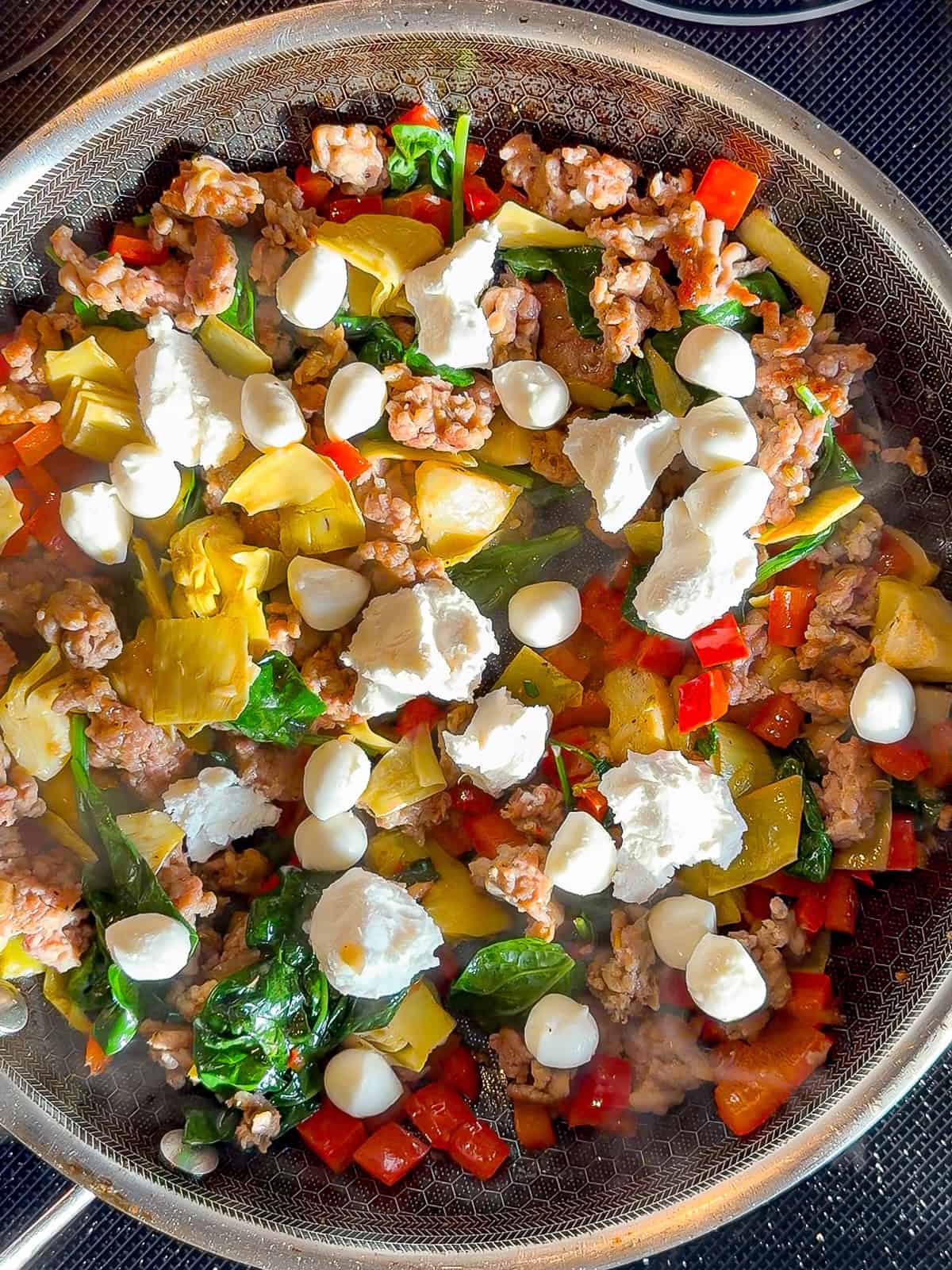 Mixed meat, vegetable vegetables, and cheese cooking in a black pan.