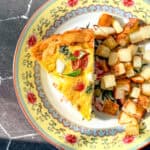 A slice of Italian frittata and cubes of roasted potato on a yellow floral plate.