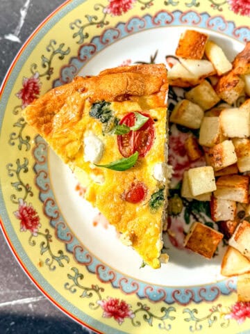 A slice of Italian frittata and cubes of roasted potato on a yellow floral plate.