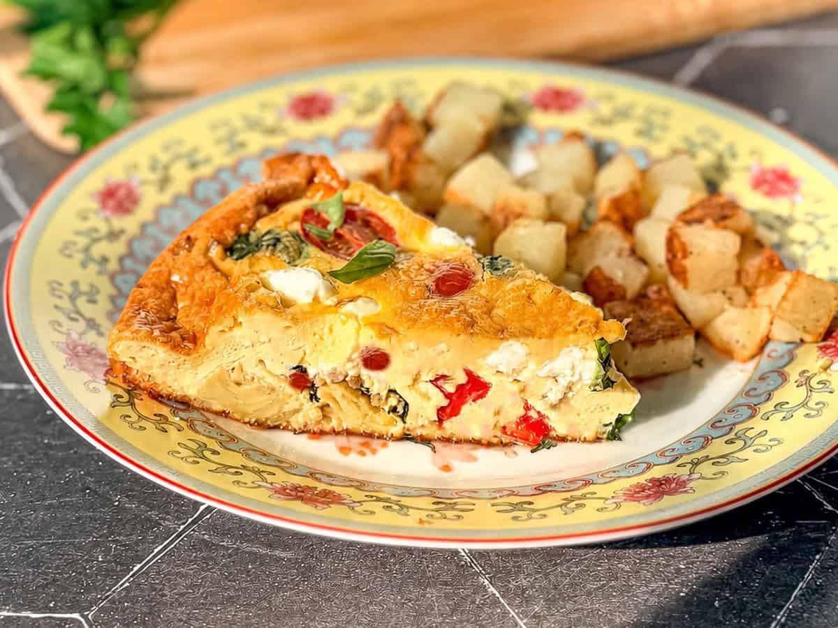 A slice of Italian frittata and cubed roasted potatoes on a yellow floral plate.