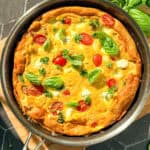 Side view of an Italian frittata and a black and silver pan on a wooden cutting board.