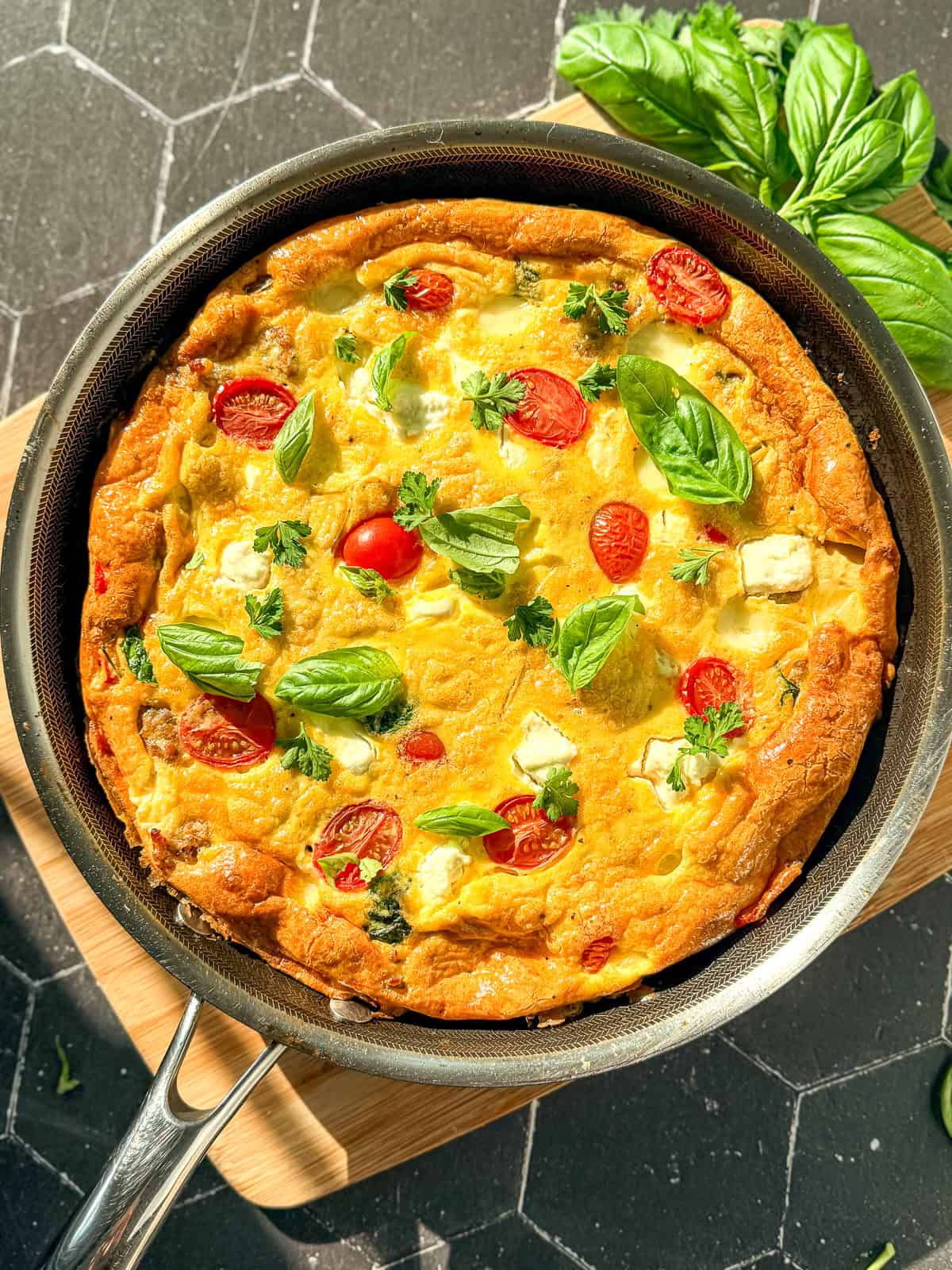 Side view of an Italian frittata and a black and silver pan on a wooden cutting board.