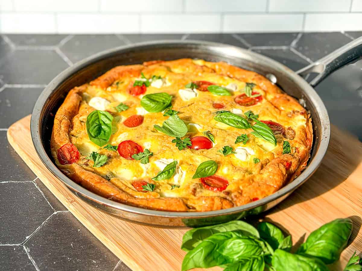 Side view of an Italian frittata and a black and silver pan on a wooden cutting board.