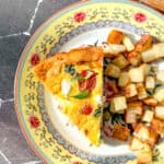A slice of Italian frittata and cubes of roasted potato on a yellow floral plate.