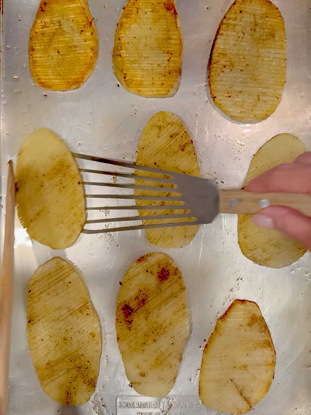 Flipping over accordion potatoes on a sheet pan.