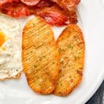 Two crispy accordion potatoes on a white plate with bacon and eggs.