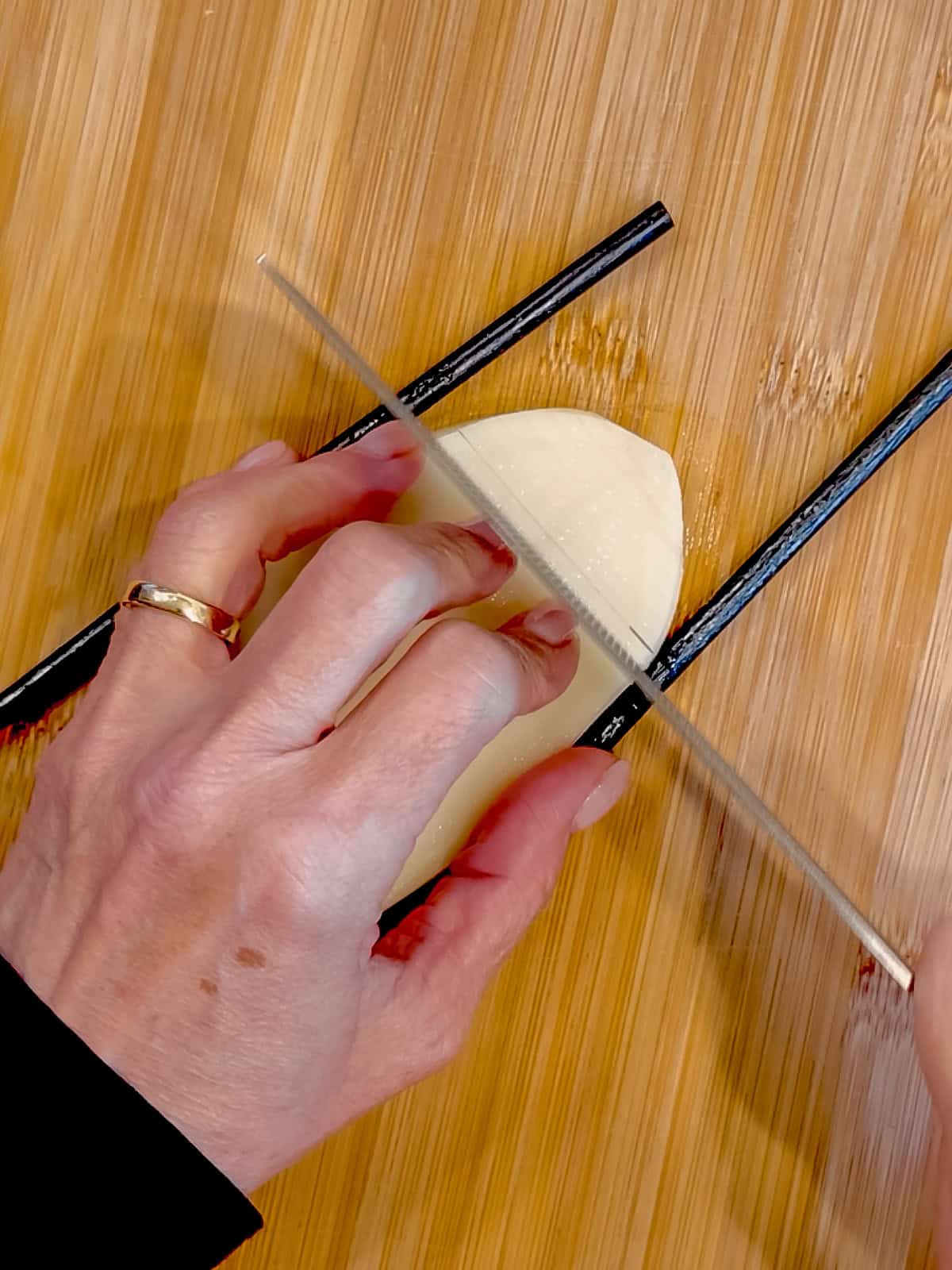 Using a knife to make thin horizontal slices on a plank of potato.