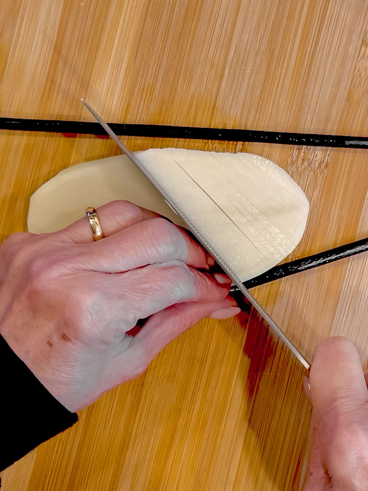Using a knife to make diagonal slices on a plank of potato.