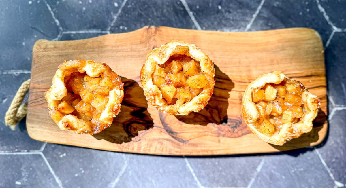 Three baked Apple croissants on a small cutting board.
