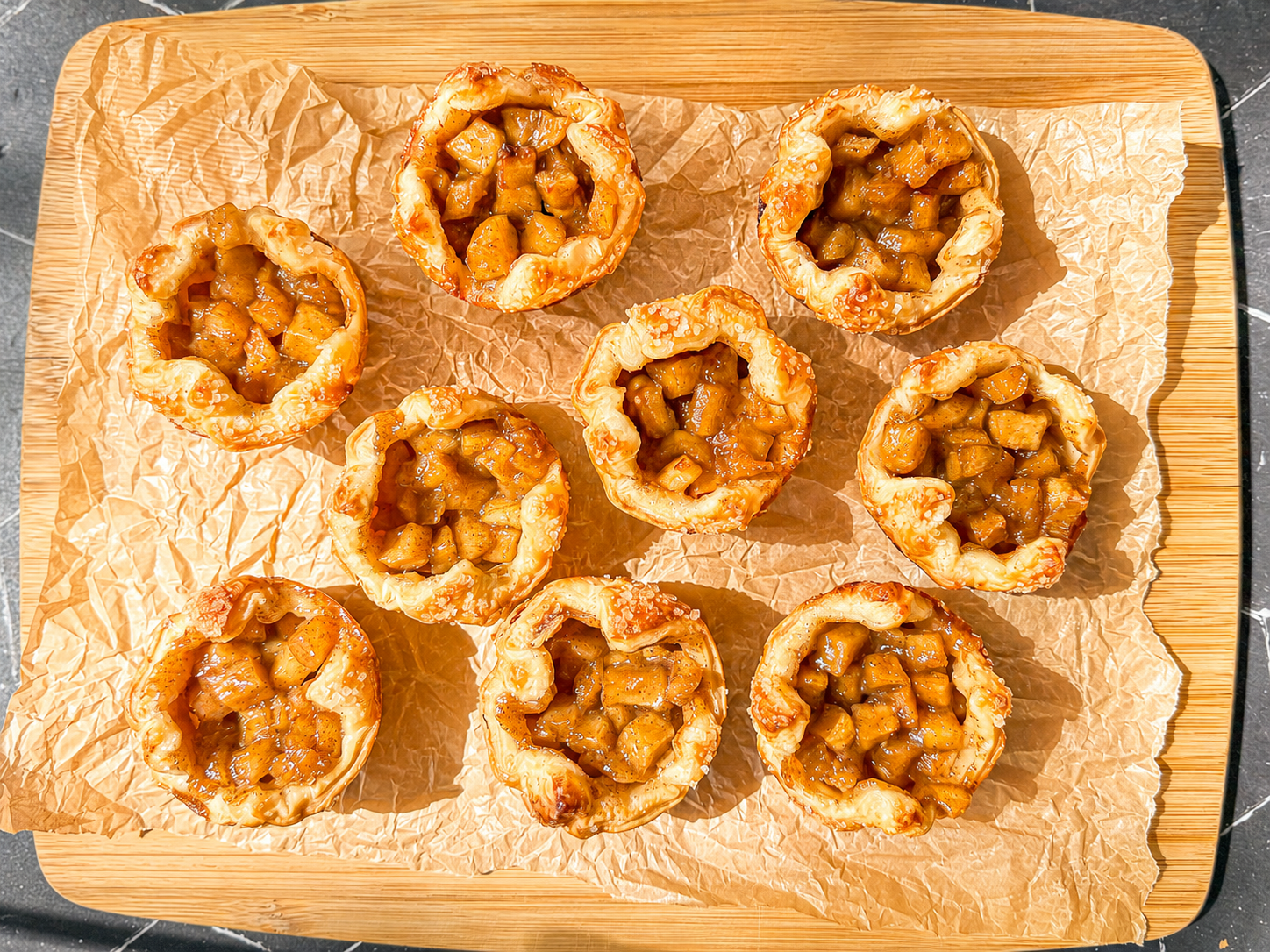 Baked apple croissants on a parchment paper covered wooden cutting board.