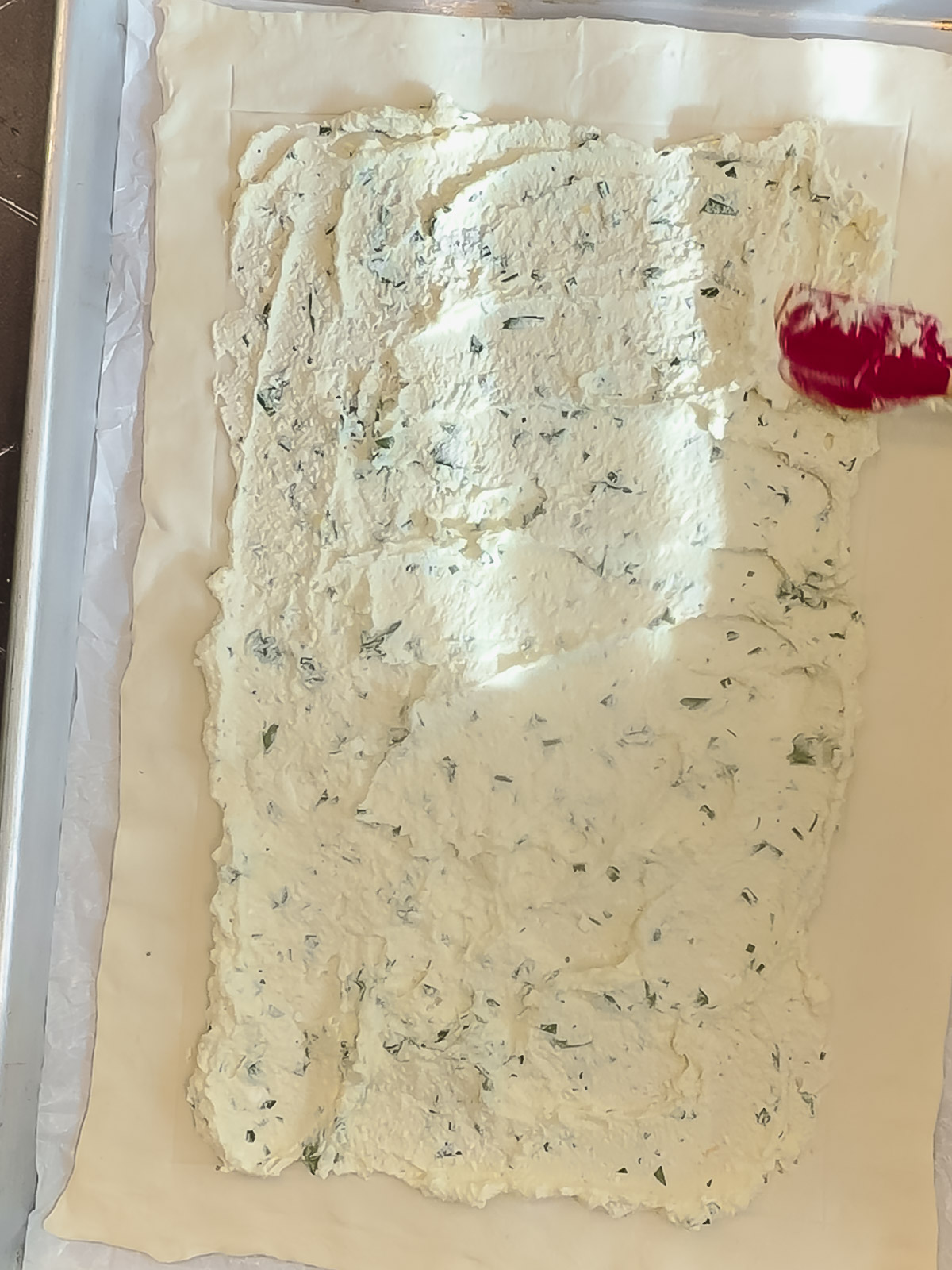 Spreading an herb ricotta filling on top of puff pastry.