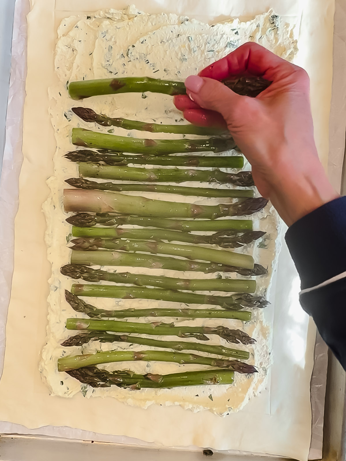 Placing asparagus spears on top of ricotta on puff pastry.