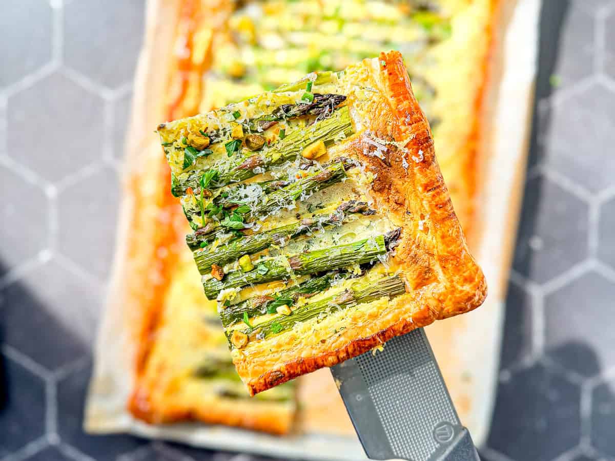 A slice of asparagus puff pastry tart on a spatula.