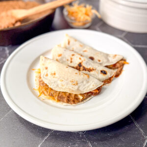Three bean and cheese tacos on a white plate.