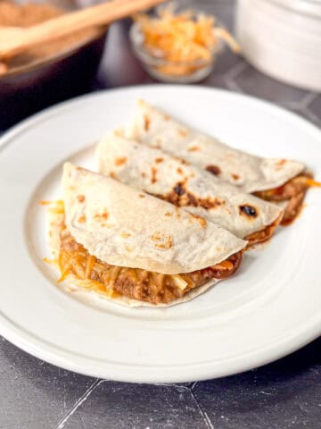 Three bean and cheese tacos on a white plate.