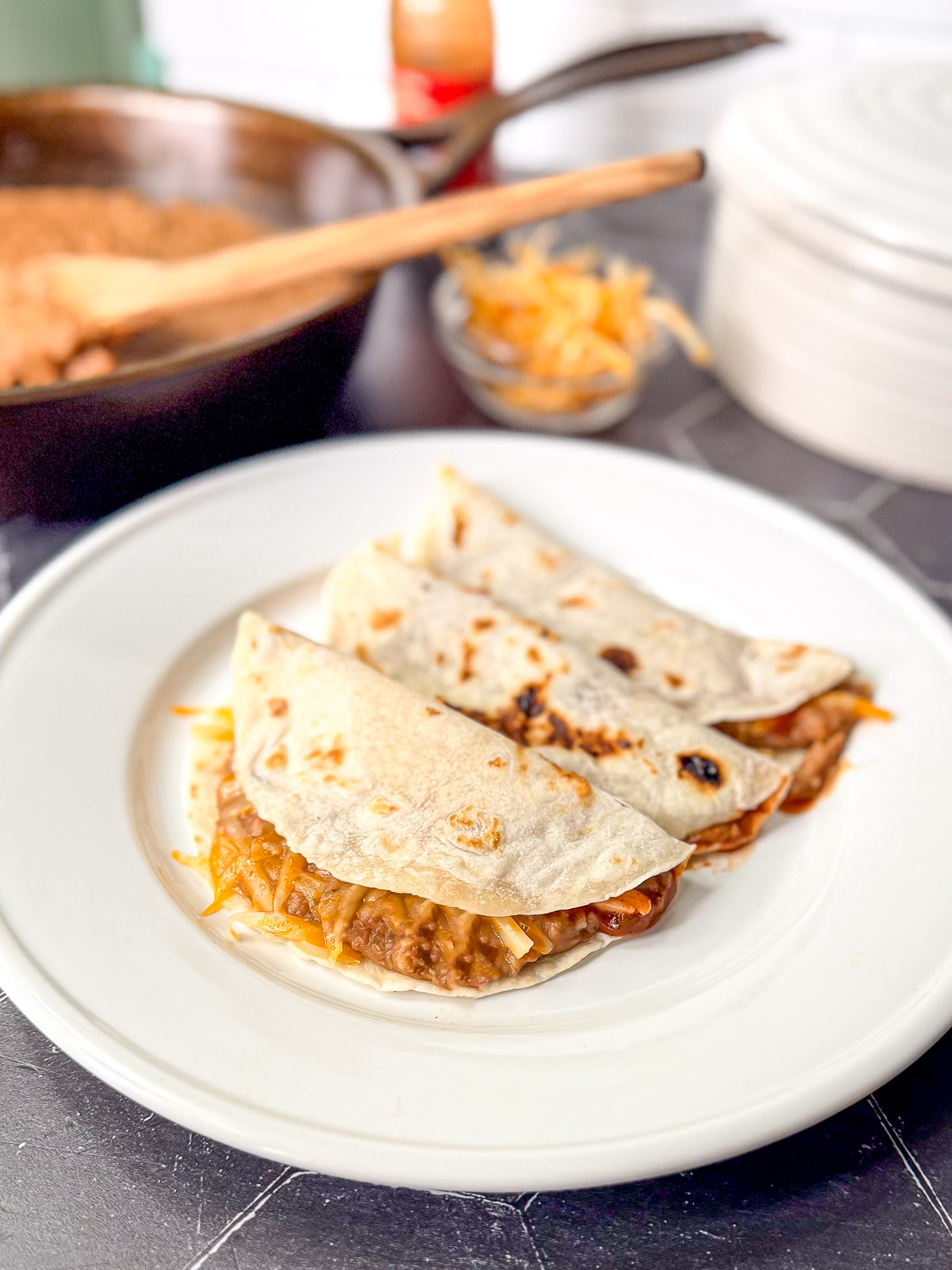 Three bean and cheese tacos on a white plate.