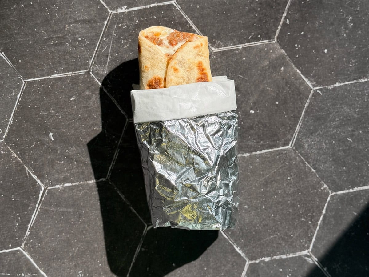 A bean and cheese taco wrapped and aluminum foil and deli paper.