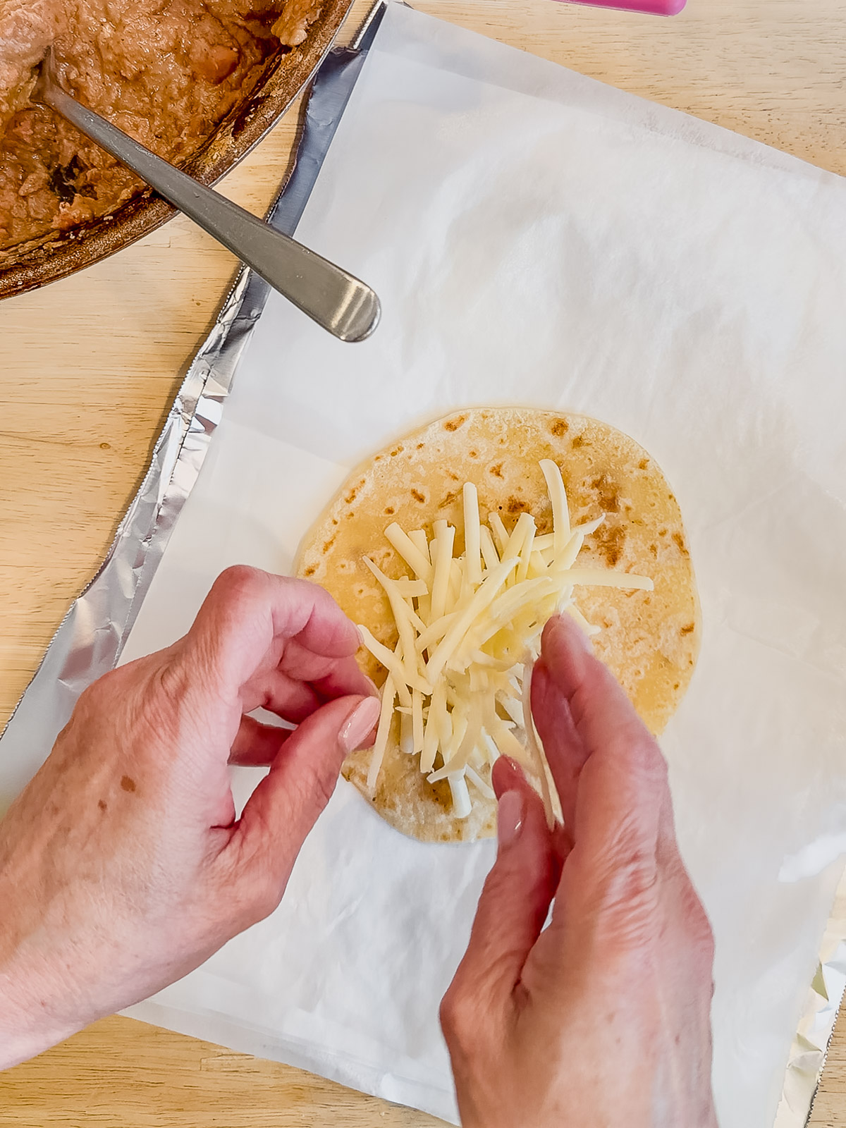 Adding shredded white cheese on top of a warm flour tortilla.