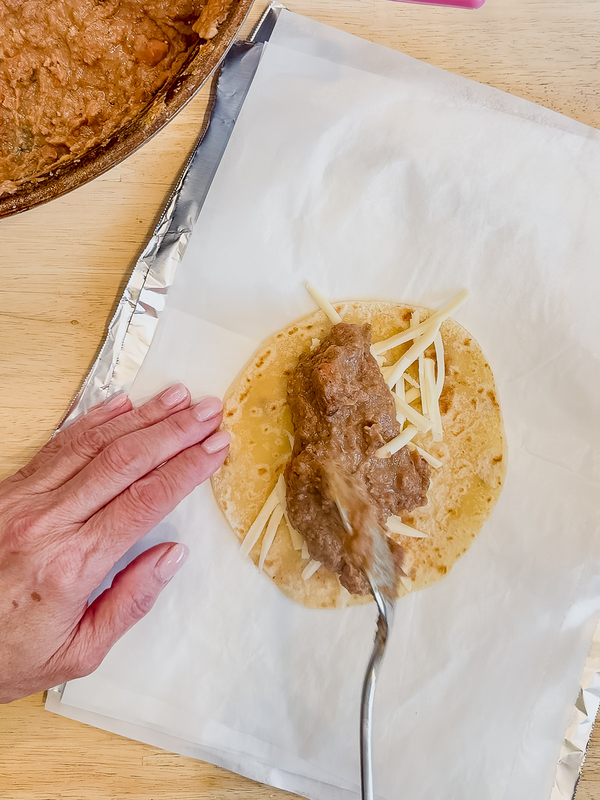 Adding a scoop of hot beans on top of shredded cheese in a flour tortilla.